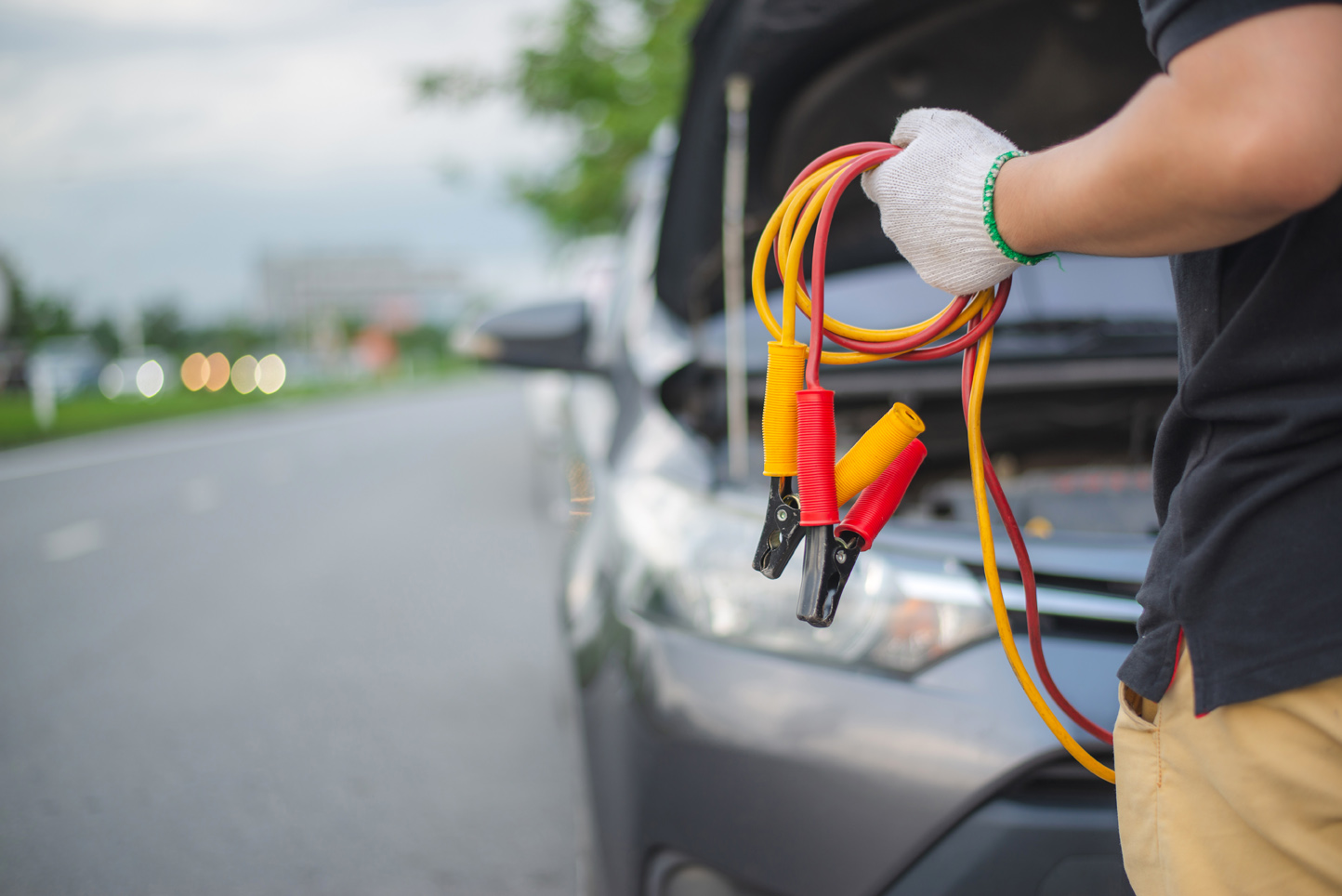 Mann hält Starthilfekabel in der Hand. Im Hintergrund ist die offene Motorhaube eines Fahrzeugs zu sehen